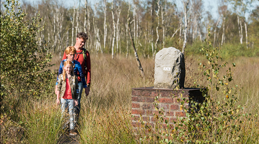 Vader en twee kinderen bij grenspaal in natuurgebied